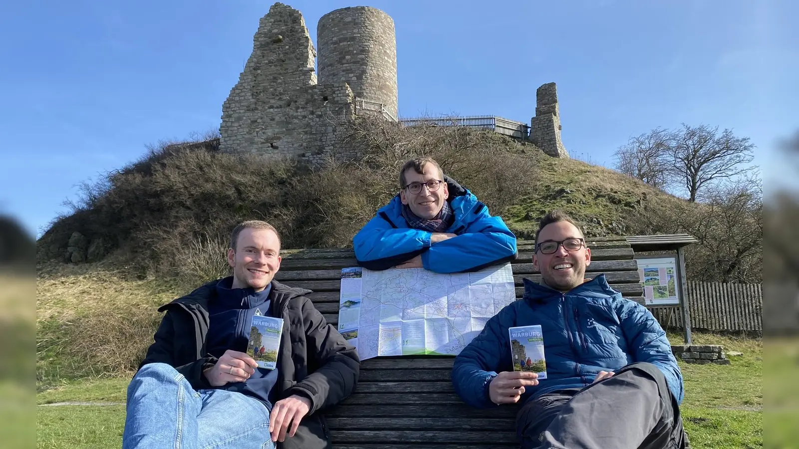 Auf dem Desenberg: (v.l.) Touristiker Lucas Lambracht, Bürgermeister Tobias Scherf und der Mobilitätsbeauftragte Jan Kolditz präsentieren bei frühlingshaftem Sonnenschein die neue Wanderkarte. (Foto: Hansestadt Warburg)