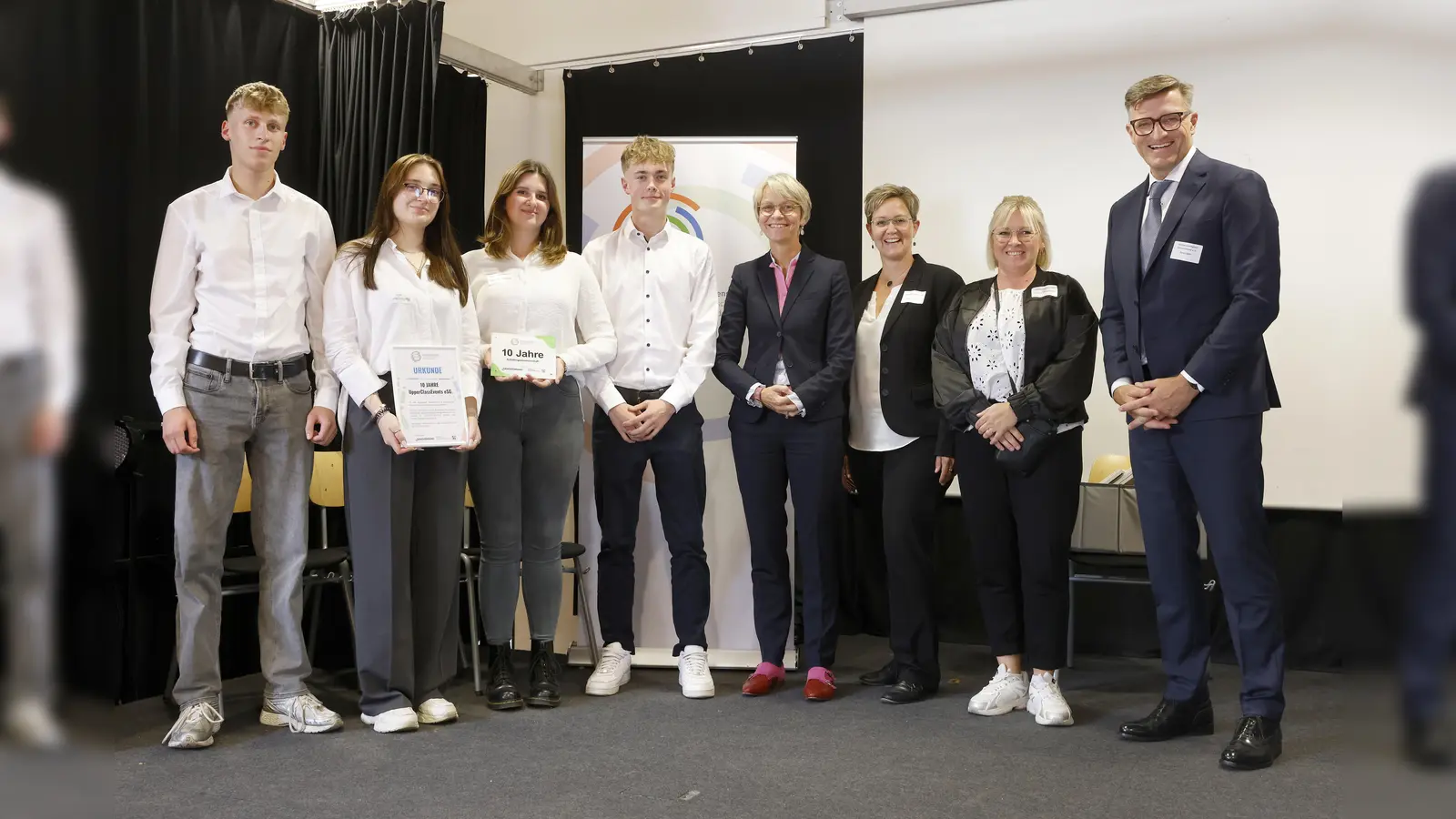 Große Freude bei der Schülergenossenschaft Upper Class Events eSG: Sie wurde am Montag, 15. September, von NRW-Schulministerin Dorothee Feller (4. von rechts) und Peter Götz, Vorstand des Genoverband e. V. (ganz rechts), für ihre erfolgreiche Arbeit in der Gesamtschule Weierheide in Oberhausen ausgezeichnet. Mit dabei waren auch (von links nach rechts) Simon Meier, Diana Shteynepreys, Vorstandsvorsitzende Samea Heinze, Stellvertreter Paul Möhrlin sowie Nadine Kohlbrock und Katja Brockhagen als begleitende Lehrkräfte. (Foto: Genoverband e. V. /Marco Stepniak)