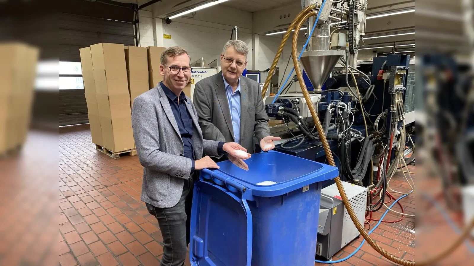 Ein Produkt - viele Möglichkeiten: Bürgermeister Tobias Scherf und Bernd Grundkötter (Geschäftsführung Tolges Kunststoffverarbeitung) betrachten das Kunststoffgranulat, das in Werkzeugformen gepresst und eingefärbt zu unterschiedlichsten Produkten verarbeitet werden kann. (Foto: Hansestadt Warburg)