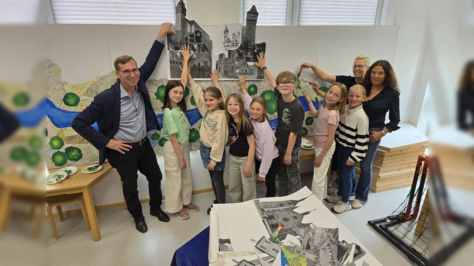 Die Schülerinnen und Schüler der 4. Jahrgangsstufe der Graf-Dodiko-Grundschule platzieren unter der Leitung von (von rechts) Anne Schäfers und Katrin Filker die charakteristischen Merkmale von Warburgs Ortschaften auf der Außenwand des Festwagens. Bürgermeister Tobias Scherf (links) zeigt sich begeistert von der kreativen Umsetzung des Mottos der „50 Jahre eine Stadt – Warburg und seine Dörfer“. (Foto: Stadt Warburg)