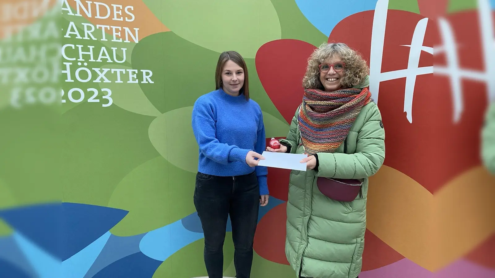 LGS-Mitarbeiterin Madita Alberding überreicht Simone Steins ihren Gewinn. Die Höxteranerin hatte den Namen „Dahlia Huxaria“ vorgeschlagen.  (Foto: LGS 2023 Höxter)