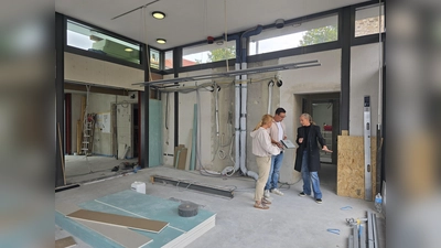 Das Herzstück des Marktplatzcafés wird die Holzrückwand im Gastraum sein. Sie wird sich künftig dort befinden, wo jetzt noch Leitungen und Rohre frei auf der Wand liegen. Silke Bergerhoff (rechts) und Katrin Micheel (links) von middel Büroeinrichtungen GmbH &amp; Co. KG planen in enger Abstimmung mit Pächter Walter Frühauf die Einbaumöbel des neuen Cafés. Die Holzrückwand ist mit speziellen Akustik-Elementen ausgestattet und wird zusätzlich zur Wohlfühlatmosphäre beitragen. (Foto: Stadt Warburg)