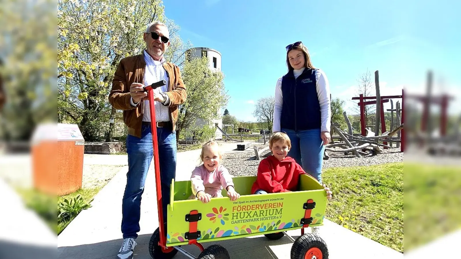 Martin Irgang vom Förderverein des Huxarium Gartenparks präsentiert gemeinsam mit Geschäftsführerin Madita Alberding die neu angeschafften Leih-Bollerwagen im Archäologiepark. Charlotte und Constantin durften als erste Probe fahren.  (Foto: Huxarium Gartenpark Höxter)
