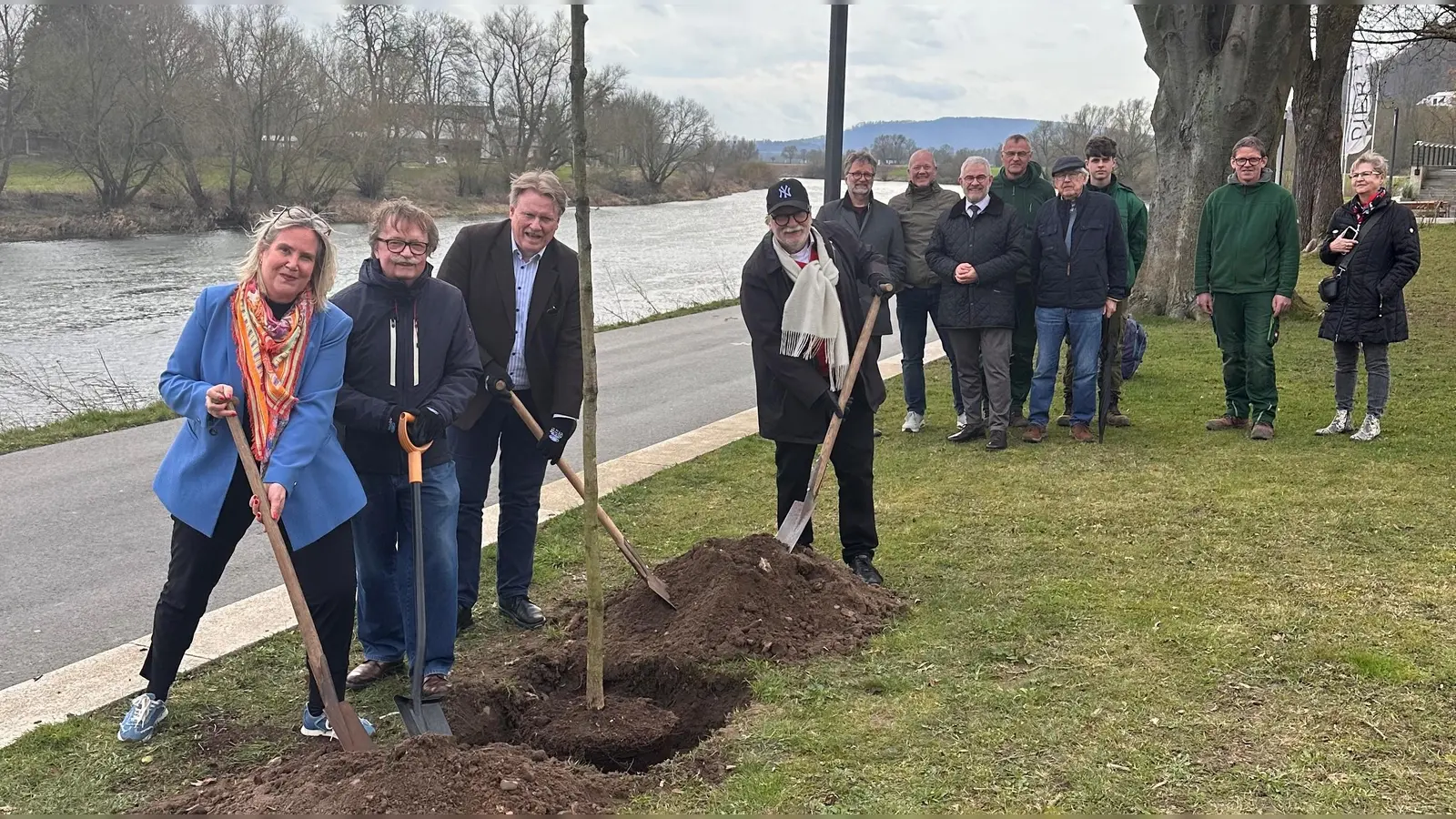 Bei der Pflanzung der Traubeneiche an der Weserpromenade (v.l.): Baudezernentin Julia Gogrewe, Norbert Drews, Vorsitzender des Heimat- und Verkehrsvereins Höxter, Matthias Köhne vom Aktionskreis zum Erhalt der Lehre am Hochschulstandort Höxter/ AFV Höxter und Stadtheimatpfleger Dirk Meyhöfer beim symbolischen Setzen des Baumes. Im Hintergrund Mitarbeitende der Stadtgärtnerei Höxter sowie weitere Unterstützerinnen und Unterstützer der Aktion „160 + 1 Bäume für den Hochschulstandort Höxter“. (Foto: Stadt Höxter)