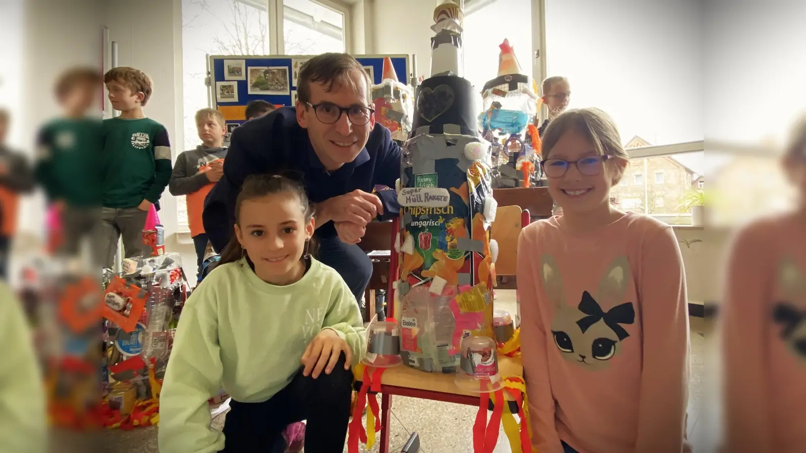 Aus Chipstüten, Puddingbechern und einem Herz aus Plastik auf dem Blumentopf: Natalia (links) und Antonia (rechts) zeigen Bürgermeister Tobias Scherf ihre Super-Müll-Rakete. (Foto: privat)