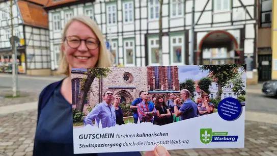 Carmen Rütters-Engemann mit dem Gutschein für die kulinarischen Spaziergänge, bei denen die Teilnehmer Warburg mit allen Sinnen genießen können. (Foto: Stadt Warburg)
