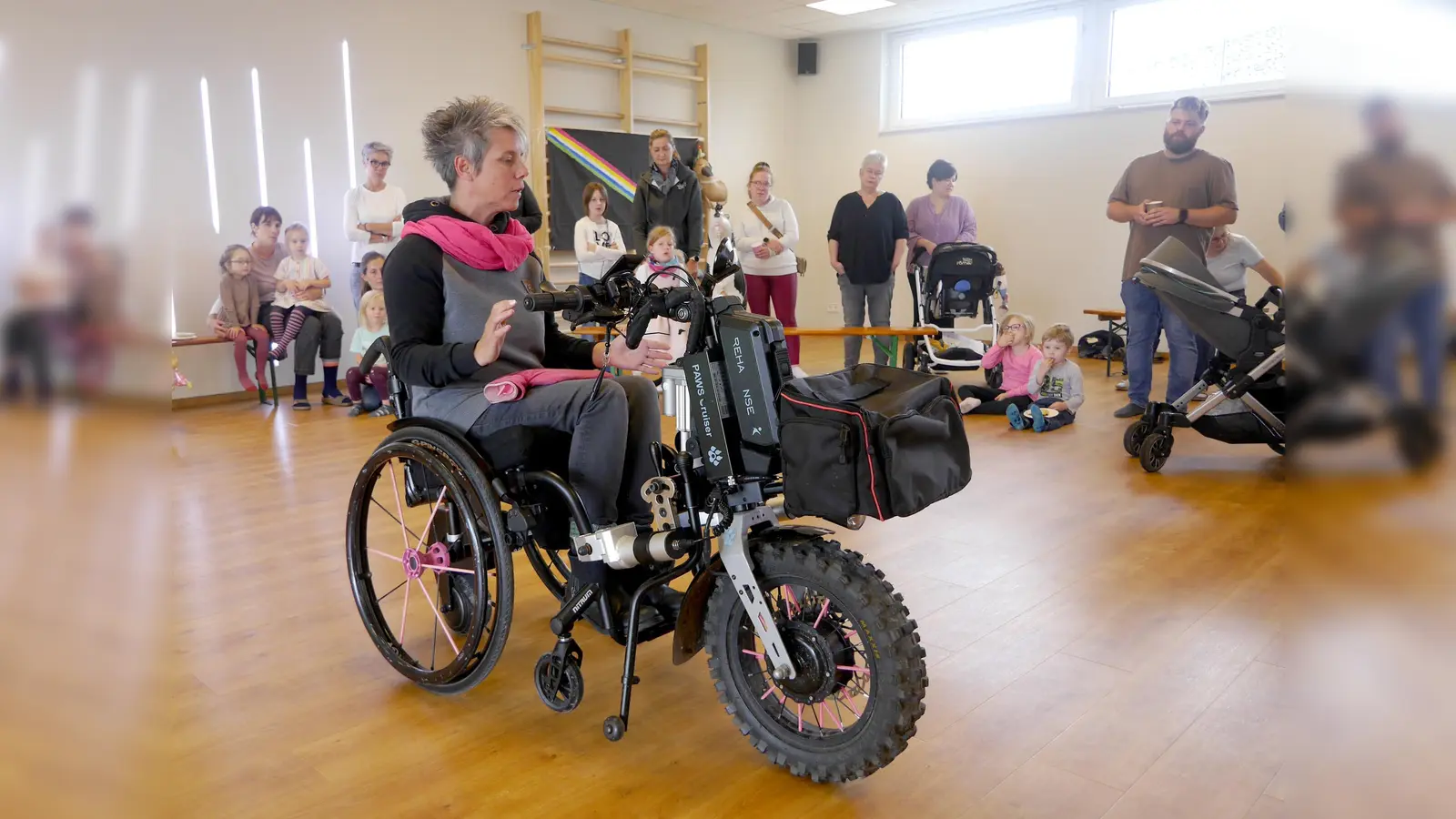 Claudia Tauchert erläutert im Gruppenraum der Kita Baumhaus in Beverungen die Funktionsweise des Zuggeräts, das sie fest mit ihrem Rollstuhl verbunden hat. (Foto: Burkhard Schwannecke)