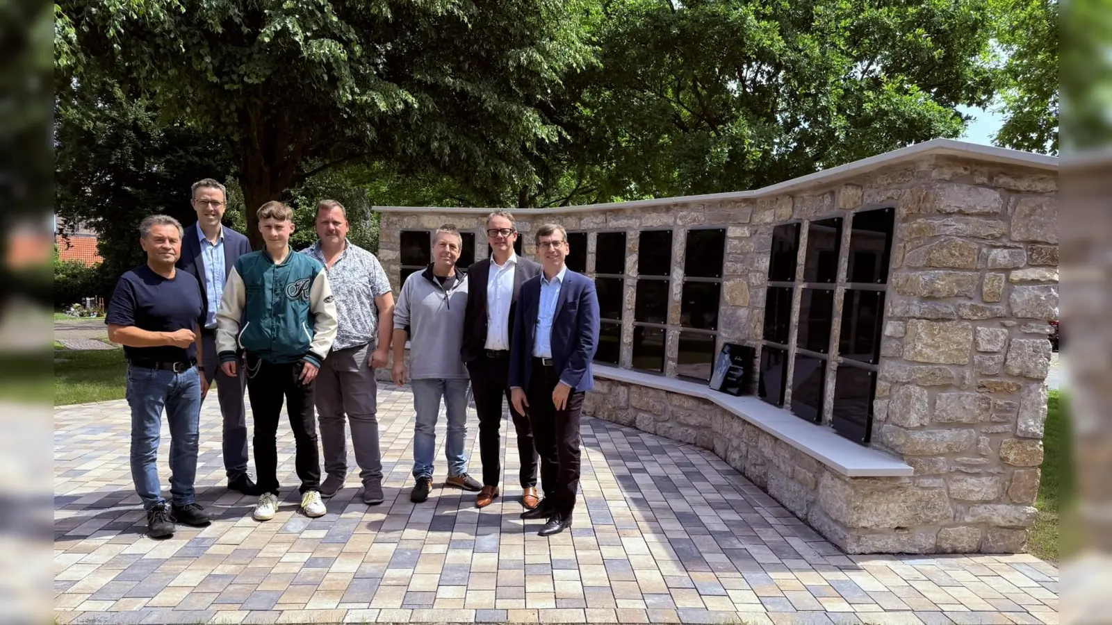 Die Bruchsteine aus den Mauern ehemaliger Dösseler Häuser prägen das harmonische Bild: Ortsvorsteher Anton Güthoff (von links), der erste Beigeordnete Andreas Niggemeyer, Tristan und Thomas Bothe (ehrenamtliche Helfer), Kurt Diesterheft (Architekt), Leander Sasse (Vorstand Kommunalunternehmen Warburg) und Bürgermeister Tobias Scherf freuen sich über die Fertigstellung der neuen Urnenmauer auf dem Dösseler Friedhof. (Foto: Stadt Warburg)