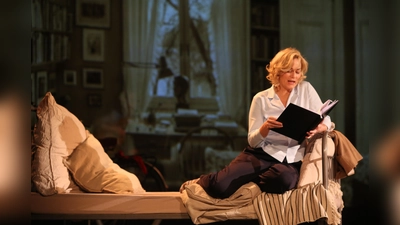 Auf einem Bett liest Gesine Cukrowski als Astrid Lindgren aus deren weltbekannten Kinderbüchern. In den Hintergrund der Bühne hat Birthe Horst das Wohnzimmer der Lindgren projiziert. (Foto: Elke Niedringhaus-Haasper)