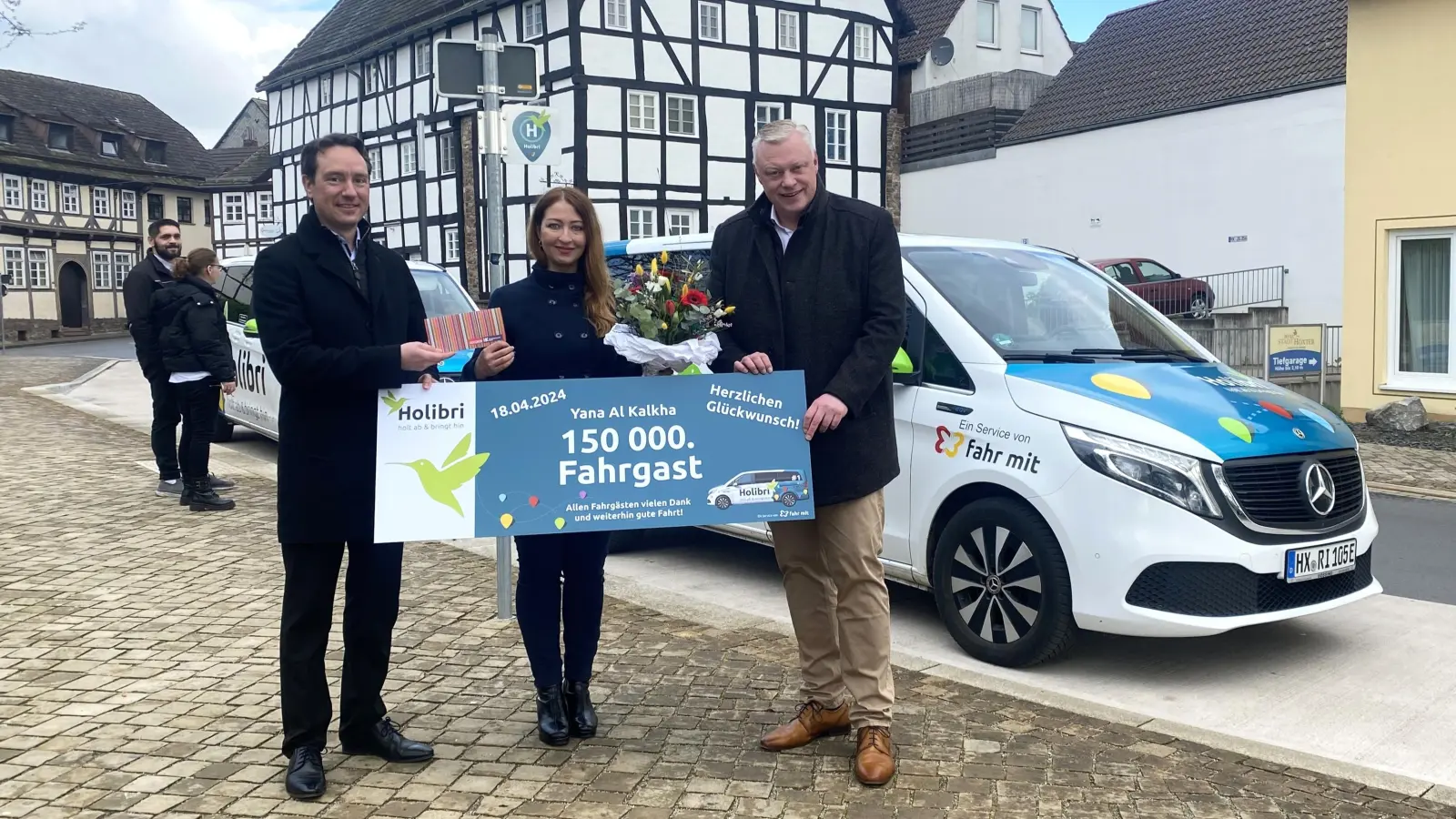 Der stellvertretende nph-Geschäftsführer Bernd Adelmeyer (links) und der Höxteraner Bürgermeister Daniel Hartmann (rechts) gratulierten der 150.000sten Nutzerin des Holibri, Yana Al Kalkha (Mitte), und überreichten ihr am Haltepunkt am Bahnhofsgelände einen Blumenstrauß mit einem Einkaufsgutschein der Werbegemeinschaft Höxter. (Foto: nph)