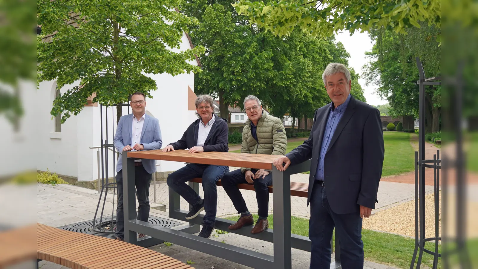 Bürgermeister Hermann Temme, Peter Frischemeier, Allgemeiner Vertreter des Bürgermeisters, Uwe Oeynhausen und Wirtschaftsförderer Alexander Kleinschmidt testen die neuen Stadtmöbel in Brakels Innenstadt. (Foto: Stadt Brakel)