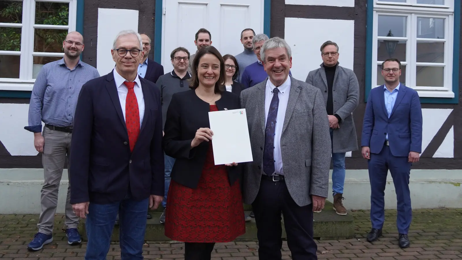 Die Detmolder Regierungspräsidentin überreicht einen Förderbescheid zur Sanierung der Meinolfushalle Bellersen (vorn v.l.): Ewald Hanisch, Bezirksausschussvorsitzender Bellersen, Regierungspräsidentin Anna Katharina Bölling und Bürgermeister Hermann Temme. (Foto: Marc Otto)