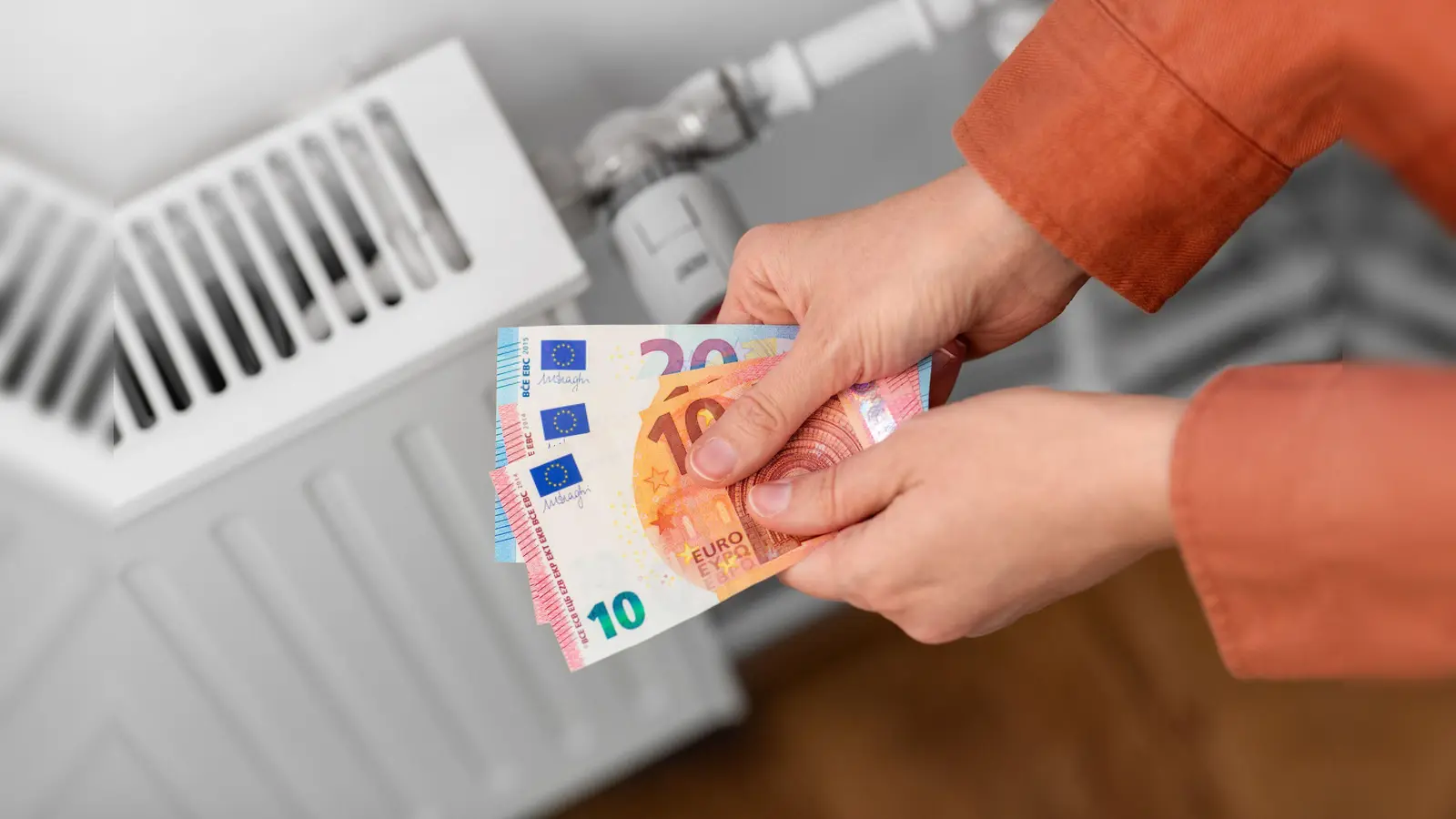 heating, energy crisis and consumption concept - close up of hands with money on radiator at home (Foto: Verbraucherzentrale NRW/adpic)