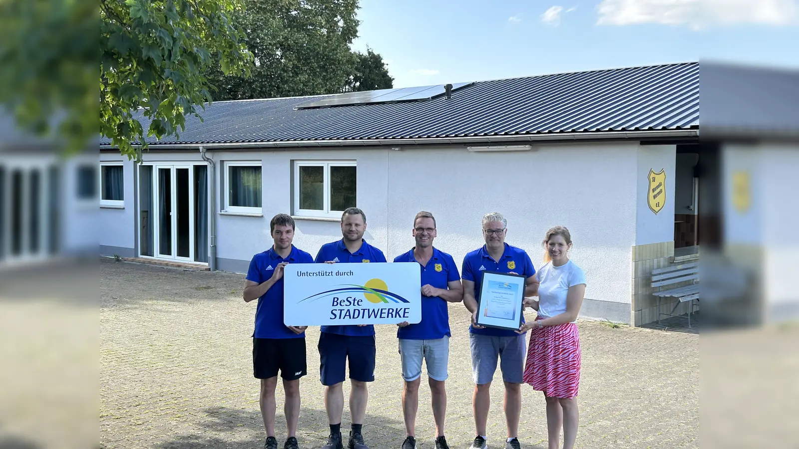 Der Vereinsvorstand (v. l.) Patrik Scholz (2. Schriftführer), Christian Thöne (2. Kassierer), Matthias Göbel (2. Vorsitzender) und Holger Dierkes (1. Vorsitzender) bedankte sich bei Julia Franzmann (BeSte Stadtwerke) für die Unterstützung und präsentierte das Balkonkraftwerk auf dem Dach des Vereinsheims (Hintergrund). (Foto: BeSte Stadtwerke GmbH)