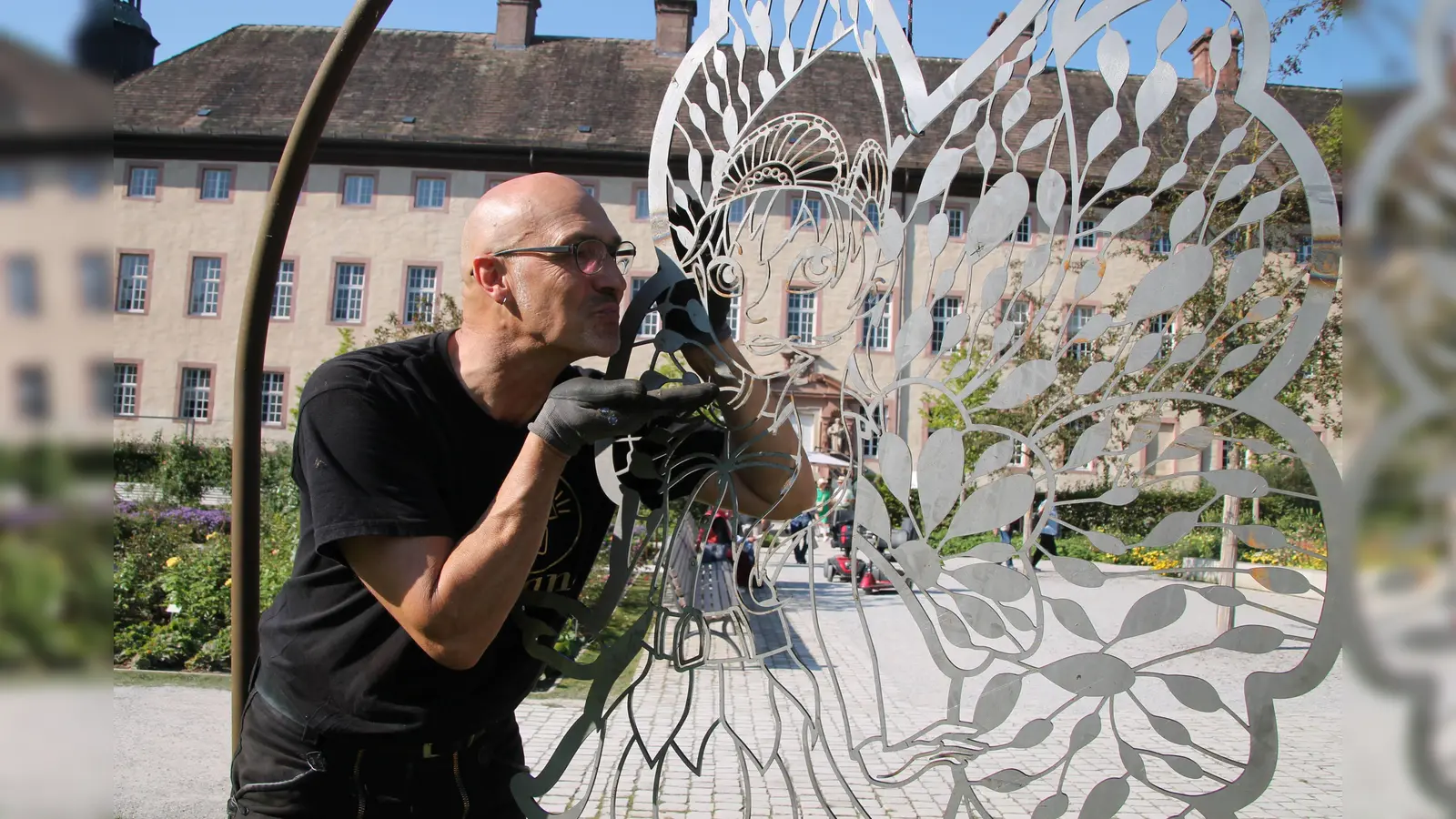 Ein Küsschen für Holli: Künstler Hans Kordes aus Verl im Kreis Gütersloh neben der stählernen Version der geflügelten Gartenschau-Botschafterin. Im Remtergarten soll die Skulptur beim Event „LightArt 2023 – Höxter leuchtet“ zu Selfies einladen. (Foto: LGS Höxter/Manuela Puls)