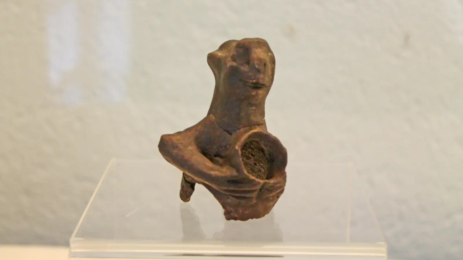 Replik der kleinen Fruchtbarkeitsfigur aus der band-keramischen Epoche der Steinzeit um 5.000 v. Chr mit vollplastischem Köpfchen und hohl getöpfertem Oberkörper. Die ursprünglich auf einem Stuhl sitzende Figur hält vor der Brust ein kleines kumpfartiges Gefäß, das mit dem Hohlkörper verbunden ist. (Foto: Kerstin Aderholz)