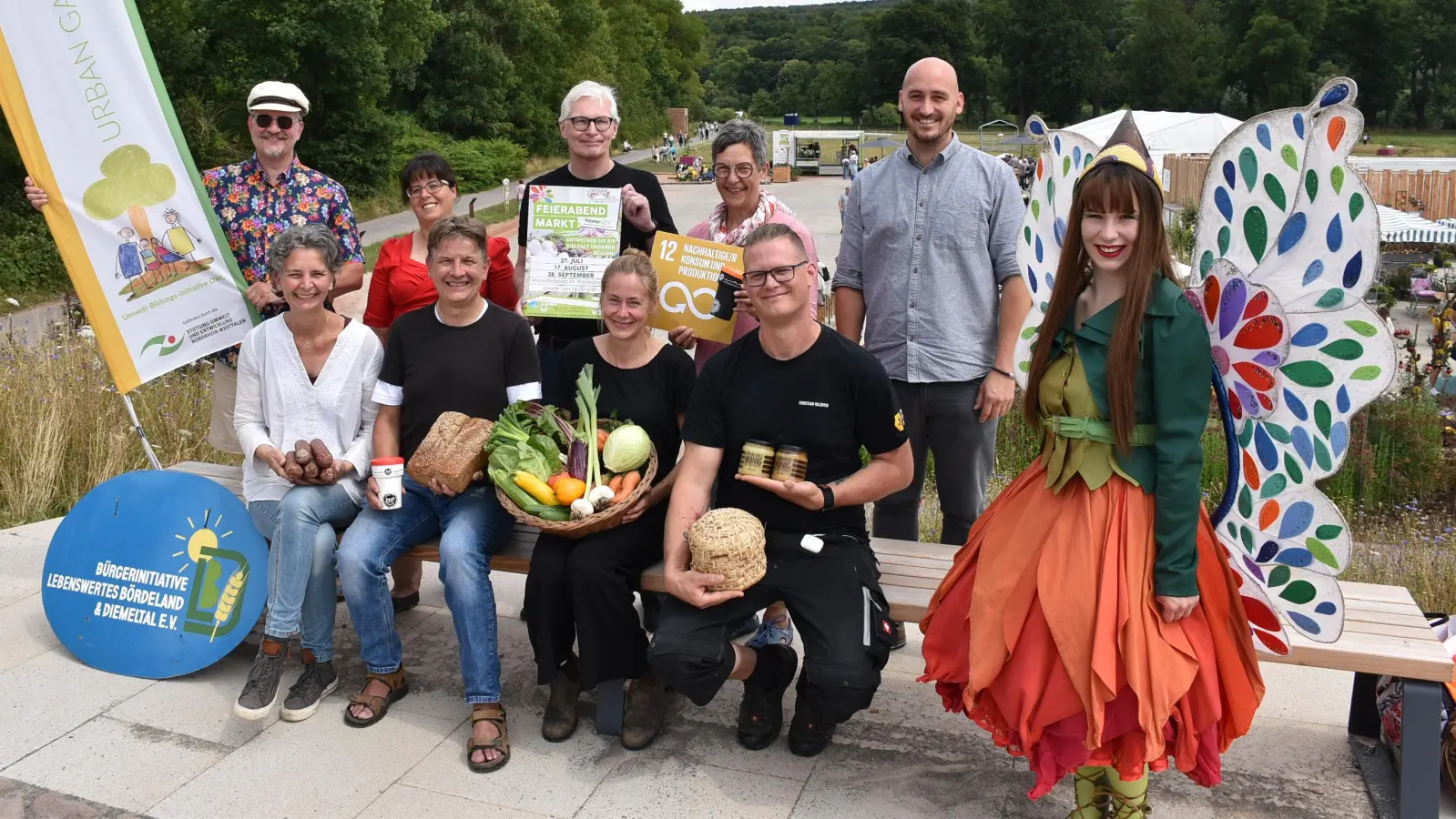 Freuen sich auf die Feierabendmärkte bei der Landesgartenschau (vorn v.l.): Jutta Sträter (Bioland-Hof Hartmann), Andreas Rode (Bäckerei Rode), Anna Lammert (Helle Bauer), Christian Valentin (Imkerei Familie Valentin) und Maskottchen Holli. Hinten (v.l.): Frederick Lüke (Umwelt-Bildungs-Initiative OWL), Claudia Koch (LGS-Geschäftsführerin), Günter Schumacher (Bürgerinitiative Lebenswertes Bördeland und Diemeltal), Martina Krog (Kreis Höxter, Abt. Umweltschutz und Abfallwirtschaft) und Jan Sommer (LGS-Geschäftsführer). (Foto: Landesgartenschau Höxter)
